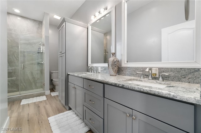 bathroom featuring hardwood / wood-style floors, toilet, decorative backsplash, a shower with door, and vanity