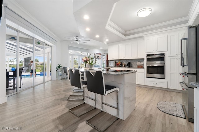 kitchen with light stone countertops, a kitchen bar, double oven, ceiling fan, and white cabinetry