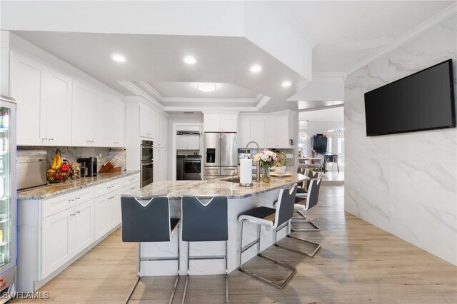 kitchen featuring light stone counters, stainless steel appliances, white cabinets, a breakfast bar area, and an island with sink