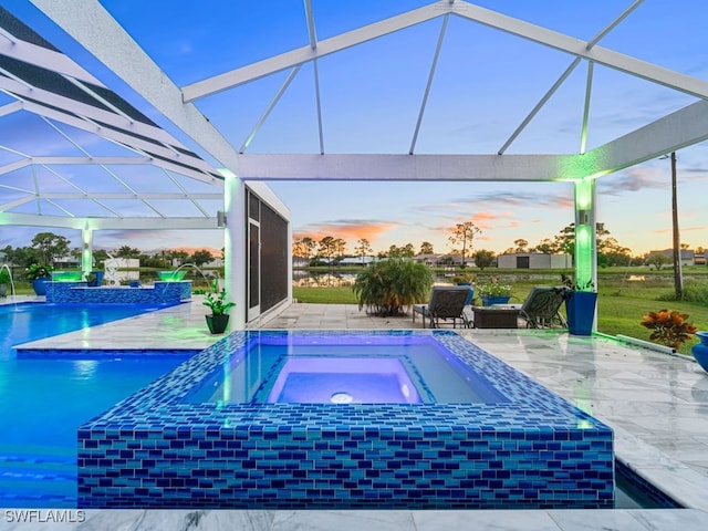 pool at dusk featuring an in ground hot tub, pool water feature, glass enclosure, and a patio area