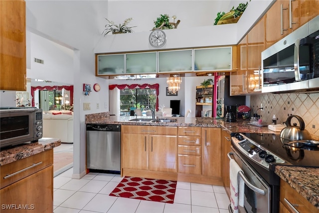 kitchen with sink, appliances with stainless steel finishes, dark stone counters, and light tile patterned flooring