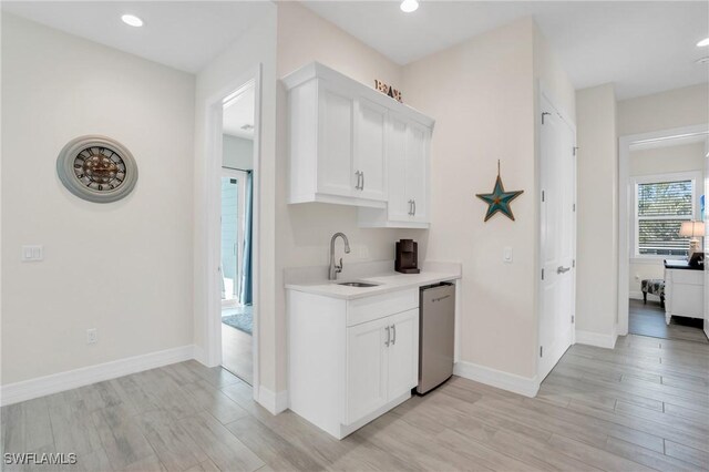 bar with dishwasher, white cabinetry, light wood-type flooring, and sink