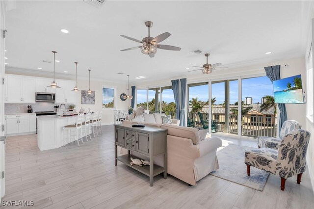 living room featuring light wood-type flooring, ceiling fan, ornamental molding, and sink