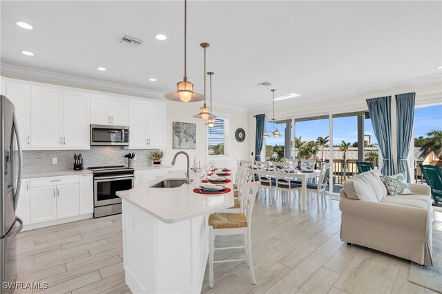 kitchen with white cabinetry, sink, stainless steel appliances, an island with sink, and decorative light fixtures