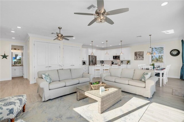 living room featuring light wood-type flooring, ceiling fan, and ornamental molding