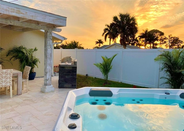 pool at dusk with a hot tub and a patio