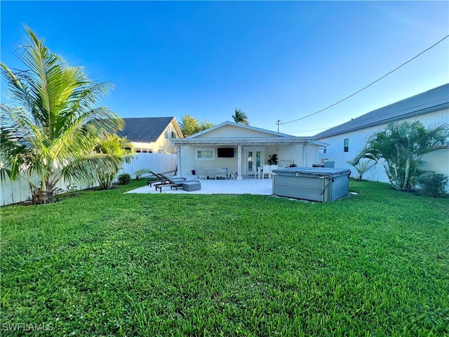 rear view of house with a hot tub, a lawn, and a patio