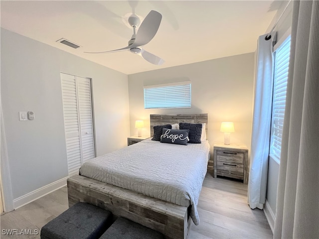 bedroom with multiple windows, light hardwood / wood-style flooring, ceiling fan, and a closet