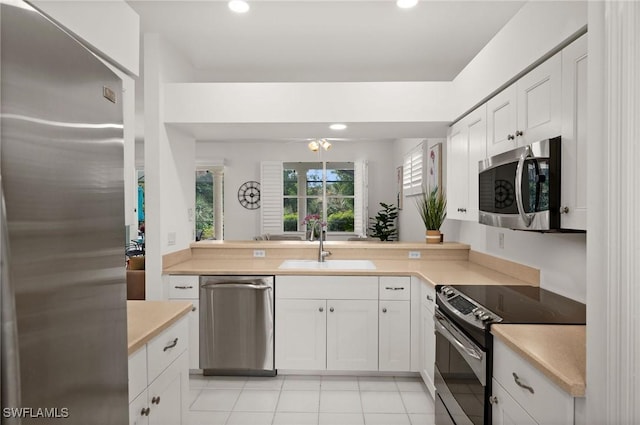 kitchen with light tile patterned floors, light countertops, appliances with stainless steel finishes, white cabinets, and a sink