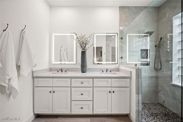 full bath featuring wood finished floors, double vanity, tiled shower, and a sink