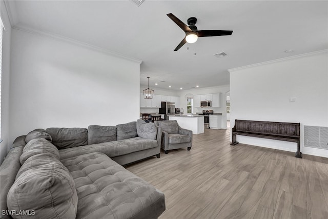 living room featuring ceiling fan with notable chandelier, crown molding, and light hardwood / wood-style floors