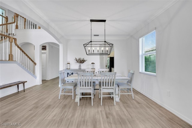 dining area with light wood-type flooring, ornamental molding, and an inviting chandelier