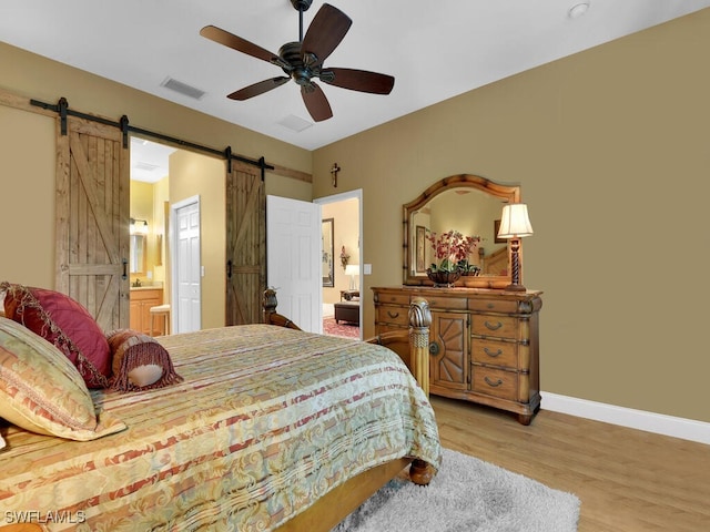 bedroom with light hardwood / wood-style floors, a barn door, ceiling fan, and ensuite bath