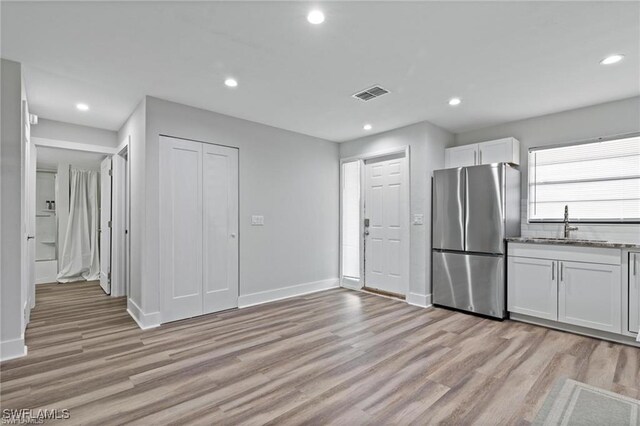 kitchen featuring stainless steel fridge, light hardwood / wood-style floors, white cabinetry, and sink