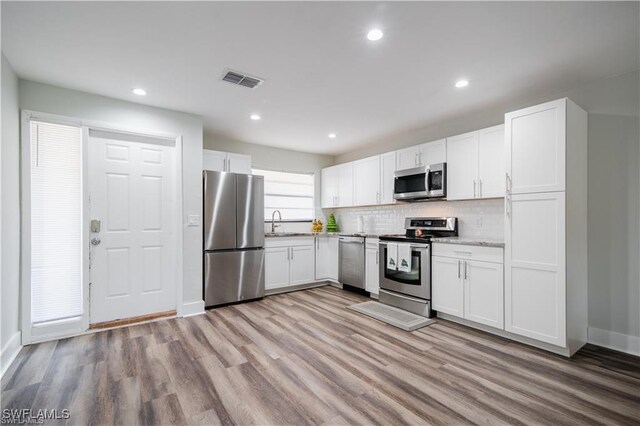 kitchen featuring stainless steel appliances, hardwood / wood-style floors, backsplash, and white cabinets