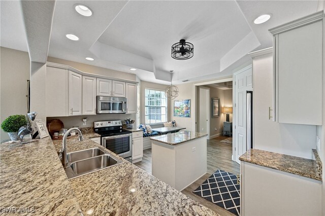 kitchen featuring decorative light fixtures, stainless steel appliances, sink, a tray ceiling, and kitchen peninsula