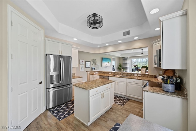 kitchen featuring a raised ceiling, light hardwood / wood-style flooring, appliances with stainless steel finishes, kitchen peninsula, and white cabinetry