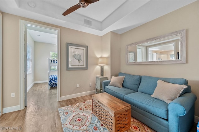 living area with light wood-type flooring, baseboards, visible vents, and a raised ceiling