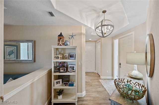 foyer with light wood finished floors, visible vents, a textured ceiling, a chandelier, and baseboards