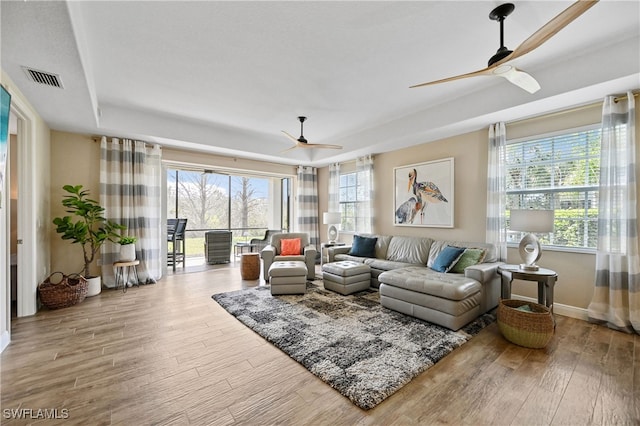 living room with a ceiling fan, a wealth of natural light, visible vents, and wood finished floors