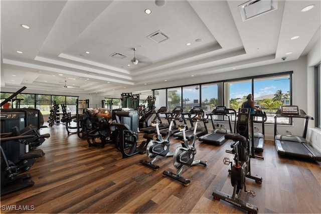 workout area with visible vents, a tray ceiling, and wood finished floors