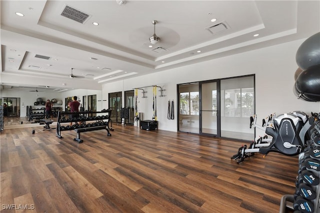 workout area featuring visible vents, a tray ceiling, a ceiling fan, and wood finished floors