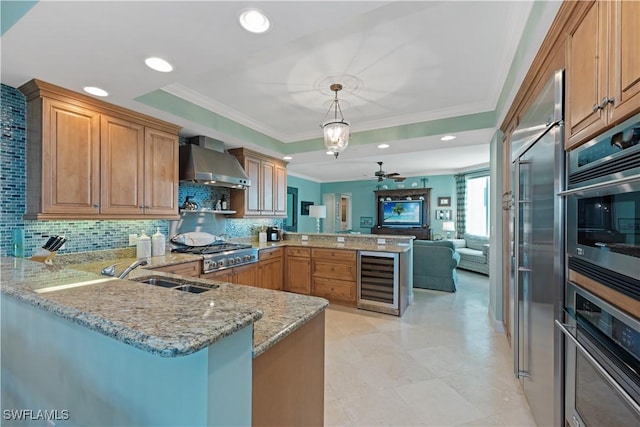 kitchen featuring a peninsula, wall chimney exhaust hood, a raised ceiling, and decorative light fixtures