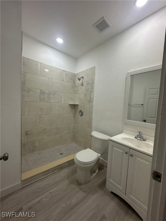 bathroom featuring a tile shower, vanity, hardwood / wood-style flooring, and toilet