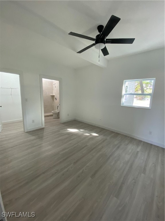 unfurnished bedroom with ensuite bath, ceiling fan, a spacious closet, wood-type flooring, and a closet