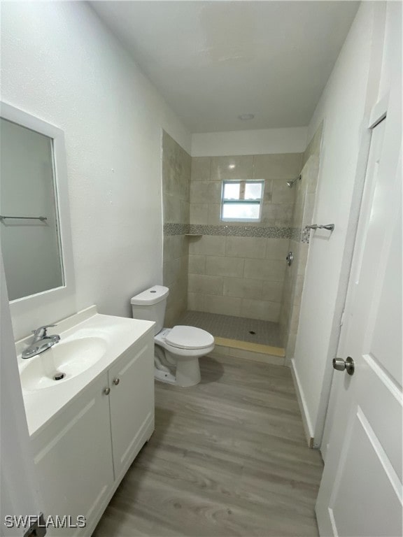 bathroom featuring a tile shower, vanity, hardwood / wood-style flooring, and toilet