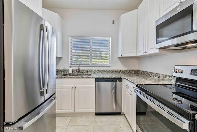 kitchen featuring sink, dark stone countertops, appliances with stainless steel finishes, light tile patterned flooring, and white cabinetry