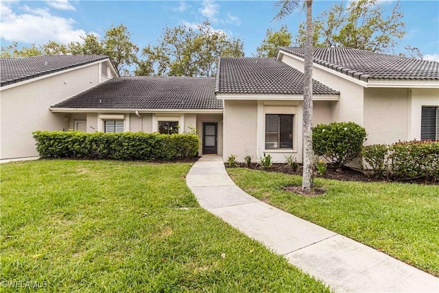 multi unit property featuring a tile roof, a front lawn, and stucco siding