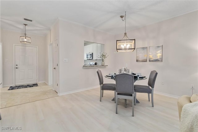 dining area featuring crown molding, a notable chandelier, light wood finished floors, visible vents, and baseboards