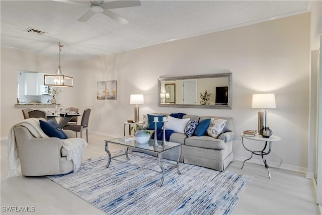 living area with visible vents, ceiling fan with notable chandelier, crown molding, and baseboards