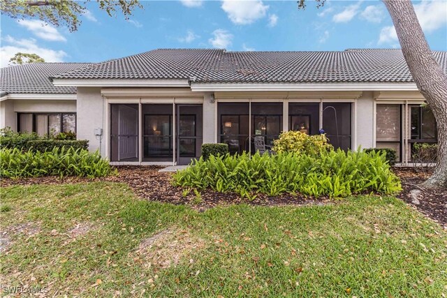 back of house with a tiled roof, stucco siding, and a lawn