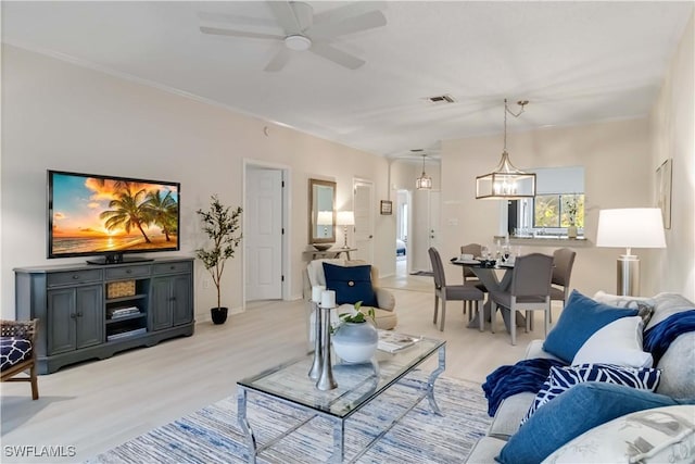 living room with visible vents, light wood-style flooring, crown molding, and ceiling fan with notable chandelier