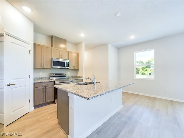 kitchen with light wood-type flooring, light stone countertops, stainless steel appliances, and an island with sink