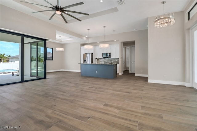 unfurnished living room featuring light hardwood / wood-style floors, sink, a tray ceiling, and ceiling fan with notable chandelier