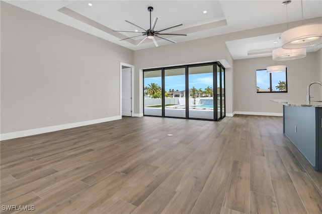 unfurnished living room with sink, hardwood / wood-style floors, ceiling fan, and a raised ceiling