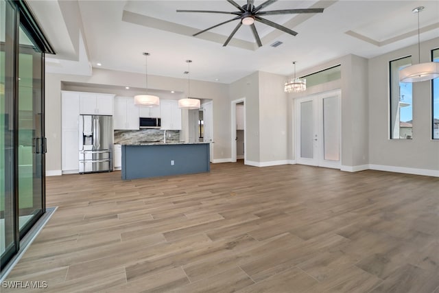 unfurnished living room featuring light hardwood / wood-style flooring, french doors, a tray ceiling, and ceiling fan with notable chandelier