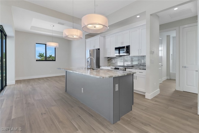 kitchen with an island with sink, white cabinets, stainless steel appliances, and pendant lighting