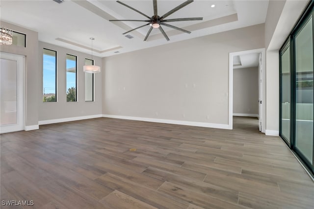 unfurnished room with wood-type flooring, ceiling fan with notable chandelier, and a raised ceiling