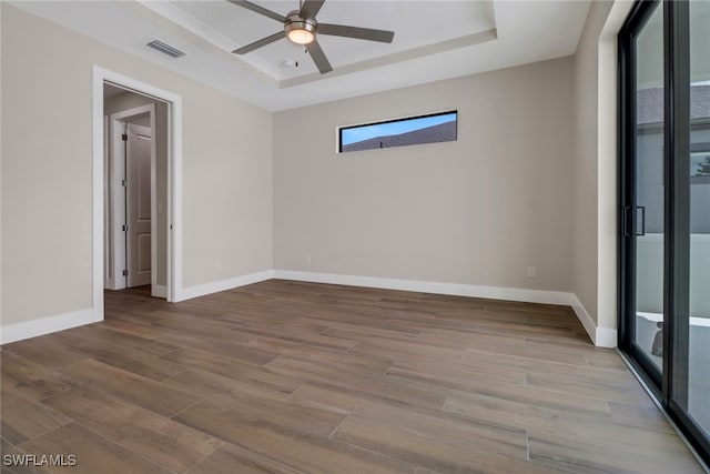 empty room with ceiling fan, light wood-type flooring, and a raised ceiling