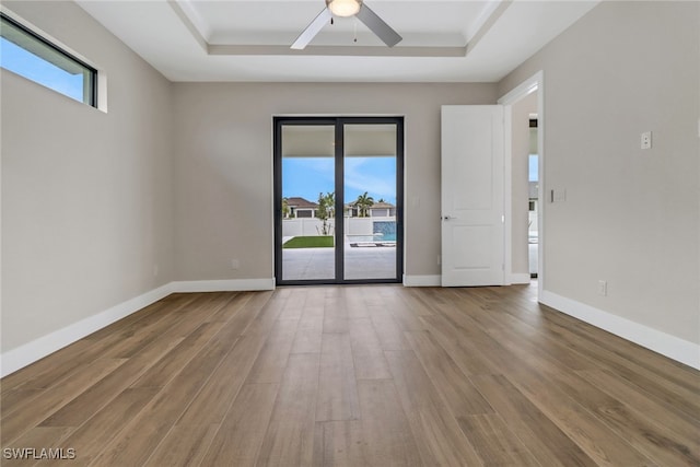 spare room with ceiling fan, wood-type flooring, a tray ceiling, and plenty of natural light