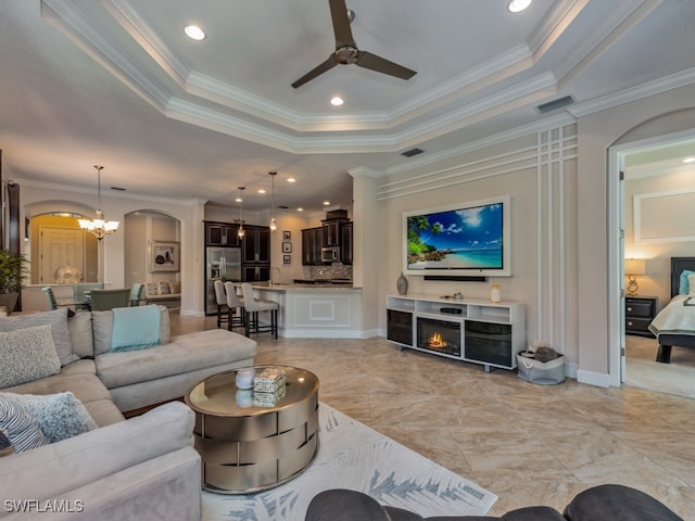 living room featuring ceiling fan with notable chandelier, ornamental molding, and a tray ceiling