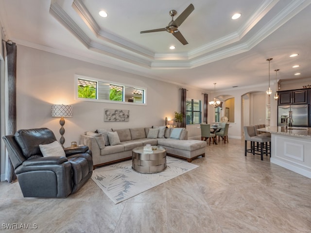 living room featuring crown molding, a raised ceiling, and ceiling fan with notable chandelier