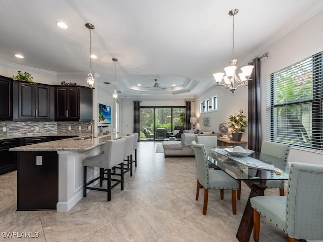 dining space featuring ceiling fan with notable chandelier, ornamental molding, a tray ceiling, and sink