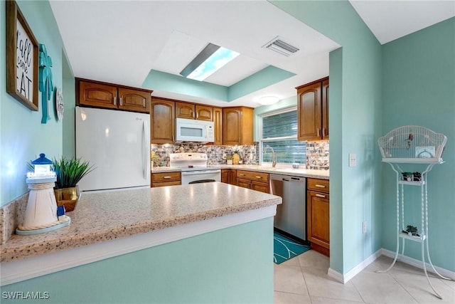 kitchen with light tile patterned floors, decorative backsplash, white appliances, light stone counters, and sink