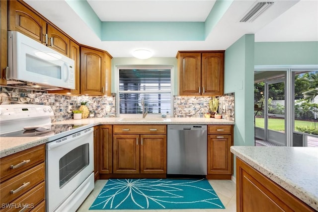 kitchen with a raised ceiling, tasteful backsplash, white appliances, light stone countertops, and sink