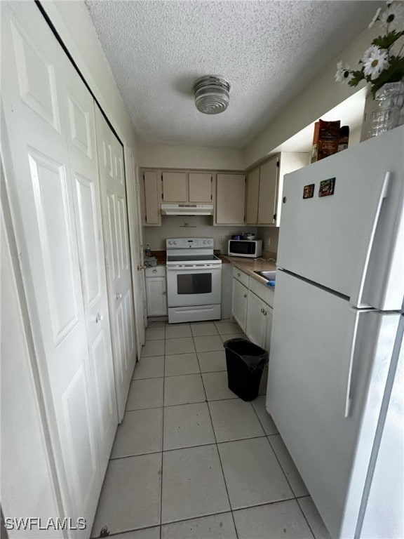 kitchen with white appliances, cream cabinets, light tile patterned flooring, and a textured ceiling